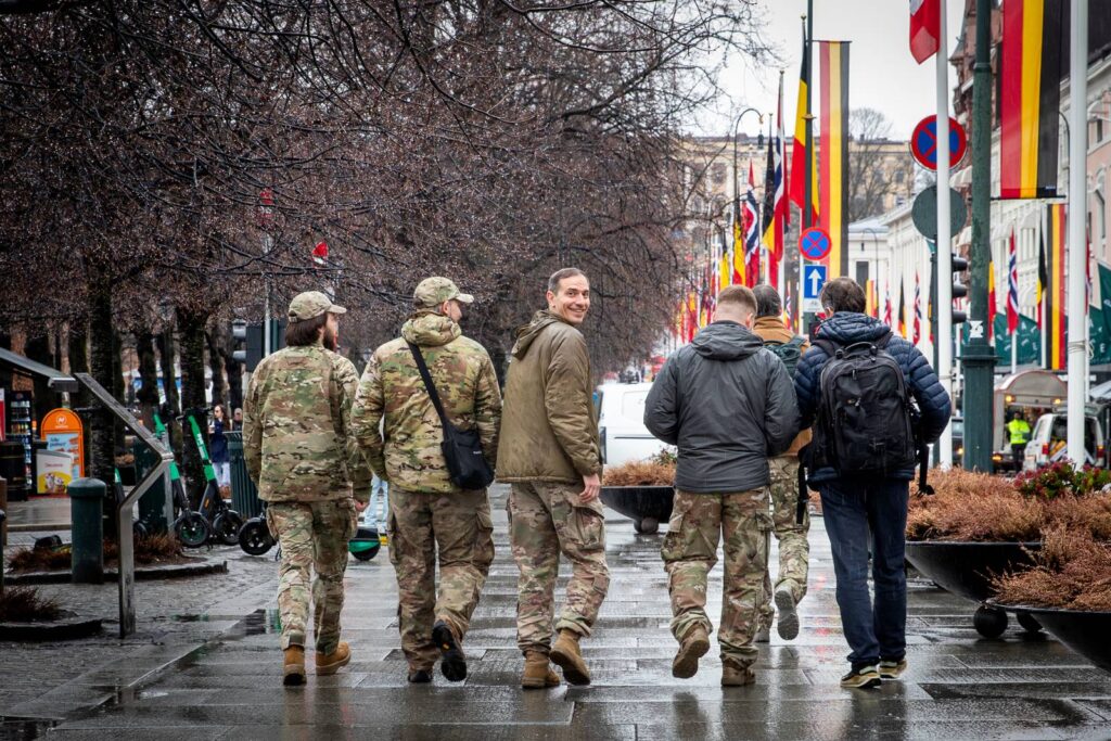 En gruppe menn, flere i militærbekledning, går nedover Karl Johans gate i Oslo. Flere ukrainske og norske flagg henger langs gaten.