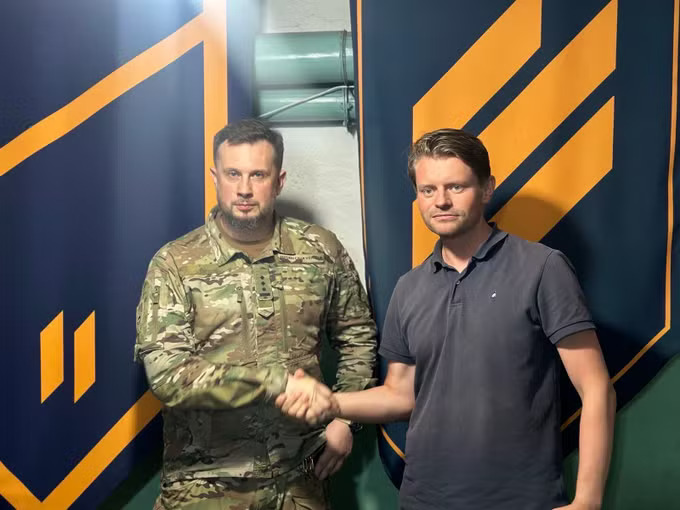 Peter Frølich fra Høyre håndhilser på Azov-grunnlegger Andrij Biletskyj foran en mørk bakgrunn med gul Azov-ss-relatert symbolikk.