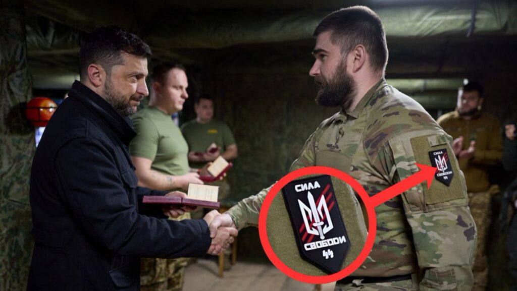 Under et besøk hos ukrainske soldater ble et merke med teksten «Сила Свободи» synlig på uniformen til en av soldatene. Symbolet er blitt omtalt som kontroversielt på grunn av likheten med SS-runer, mens enheten selv hevder at det viser tallet 44. Foto: skjermdump / bearbeidet bilde fra sosiale medier