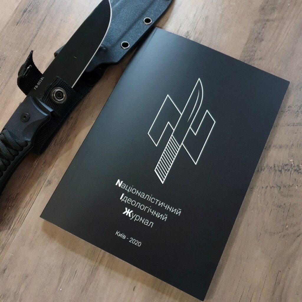 Svart hefte med ukrainsk tekst og et hvitt nasjonalistisk symbol på forsiden ligger på et trebord ved siden av en svart kniv.